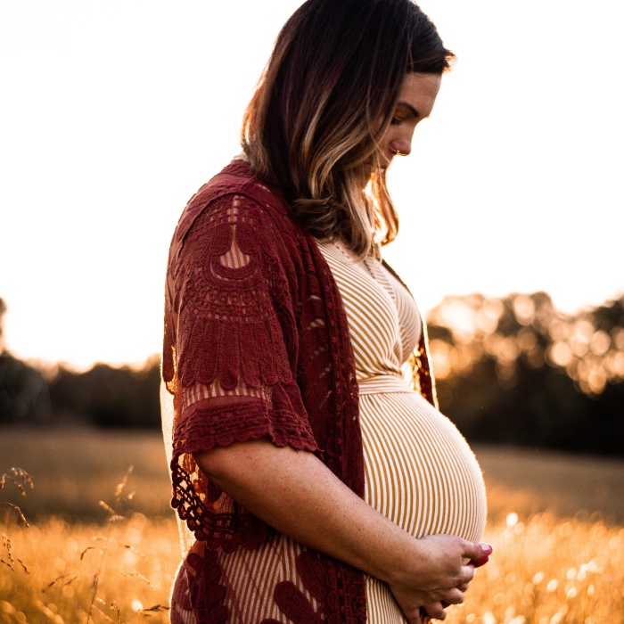 An expecting mother backlit by the sun, caressing her belly