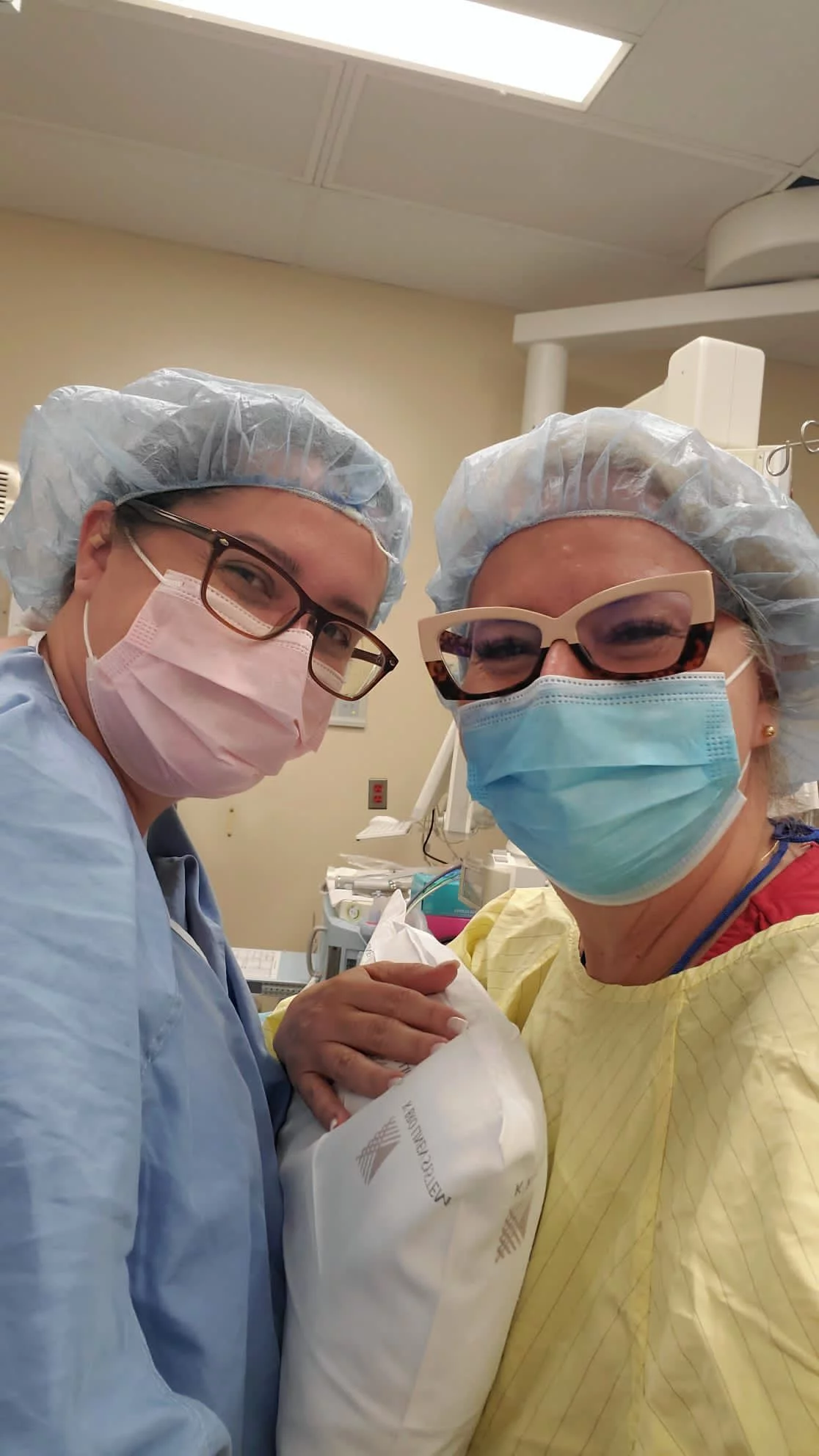 A photo of a new mother and Marcia standing in a hospital with masks and gowns on
